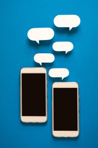Smartphones with paper speech bubbles on blue background. Communication concept. Top view. Copy space. Paper composition
