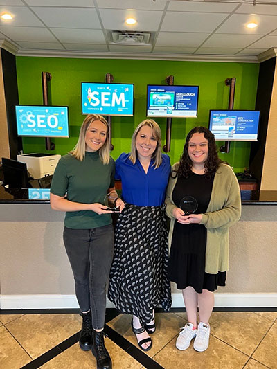 Social media marketing team members with Meta Marketing Certification awards. Front lobby of the Ocala office building.